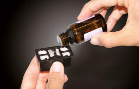 Hände halten eine braune Duftölflasche und eine schwarze Duft-Filtereinheit. Ideal für Luftreiniger und Klimatechnik.