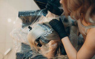 Friseurin mit Schutzmaske und Handschuhen, die das Haar einer Kundin färbt