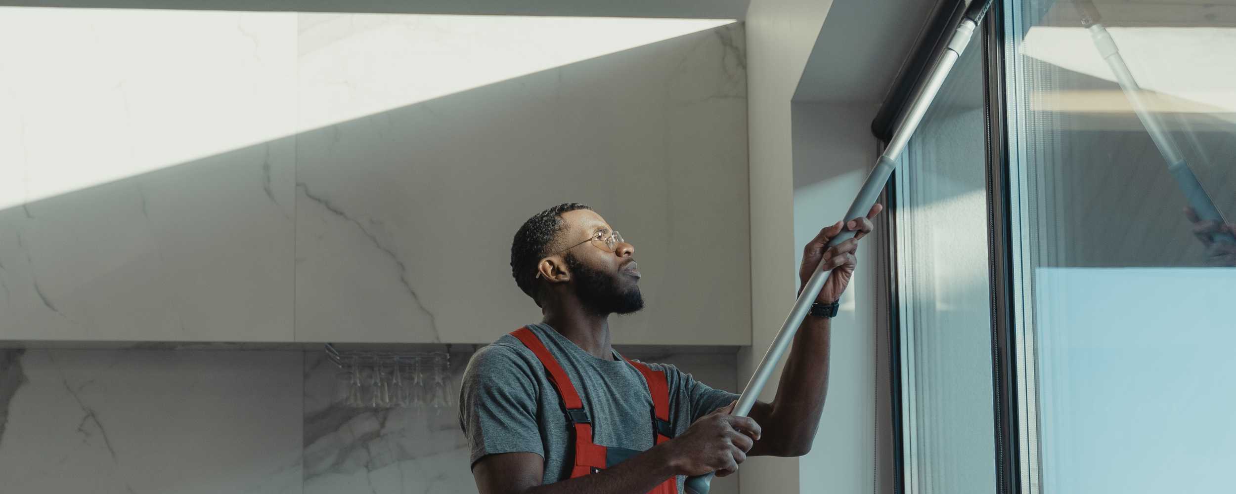 Mann putzt Fenster mit Abzieher. Fensterreinigung für saubere Scheiben. Professionelle Reinigungskraft für streifenfreie Fenster.