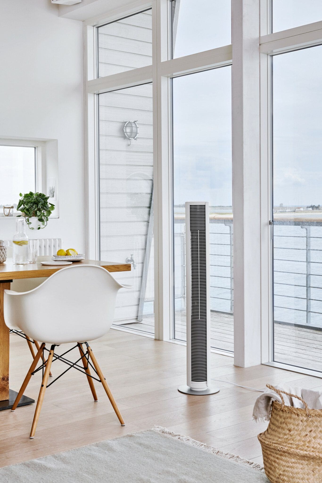 Heller Wohnraum mit Peter White Turmventilator. Lifestyle-Szene mit Stuhl, Tisch und Blick auf das Meer. Modernes Design.