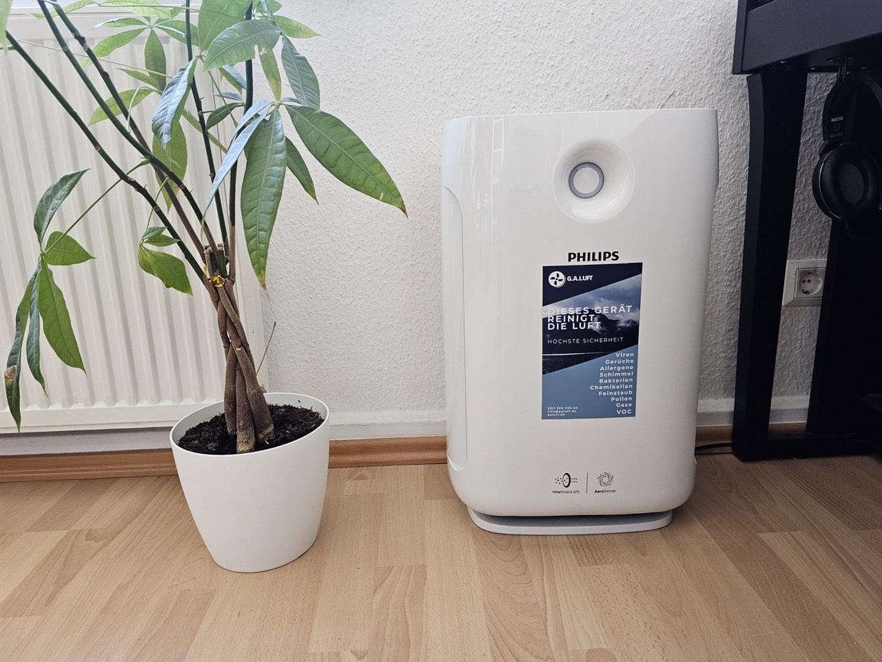 Das Foto zeigt den Philips 2000 Series Luftreiniger AC2887/10, ein elegantes und modernes Gerät, das speziell für große Räume konzipiert ist. Das in einem stilvollen Weiß gehaltene Gehäuse verleiht dem Luftreiniger eine saubere und minimalistische Ästhetik, die sich nahtlos in jedes Interieur einfügt. Im Vordergrund des Luftreinigers befindet sich der Luftqualitätssensor, ein Schlüsselelement dieses Modells, der die Luftqualität in Echtzeit überwacht und anzeigt. Die Farbcodierung auf dem Display informiert den Benutzer schnell über die Luftqualität im Raum, wobei Blau für gute und Rot für schlechte Luftqualität steht. Das Gerät verfügt über mehrere Filterstufen, darunter ein HEPA-Filter, der bis zu 99,97% der Allergene und Partikel bis zu einer Größe von 0,3 Mikrometern entfernen kann. Der große Lufteinlass und -auslass sind strategisch platziert, um eine optimale Luftzirkulation zu gewährleisten. Mit seinen schlanken Abmessungen und dem ergonomischen Griff bietet der Philips Luftreiniger AC2887/10 eine Mischung aus Funktionalität und Stil und stellt eine effiziente Lösung dar, um eine gesündere und angenehmere Umgebung in Ihrem Wohnraum zu schaffen.