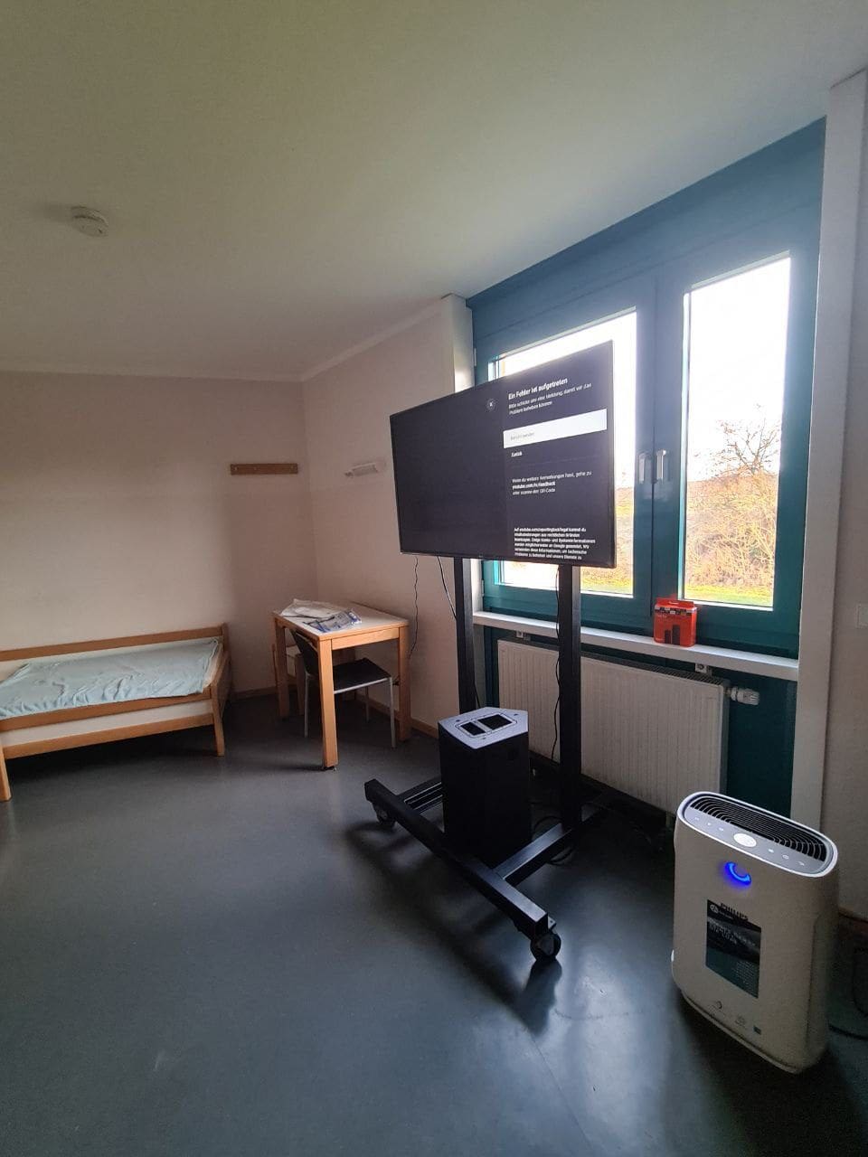 Zimmer mit Philips AC2889 Luftreiniger, Bett, Tisch, Fernseher am Fenster. Luftreiniger verbessert Raumluftqualität.