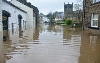 Starkregen Überschwemmung: Überflutete Straße in einer Stadt nach Unwetterschäden. Gebäude und Kirche spiegeln sich im Wasser. Chris Gallagher Foto.