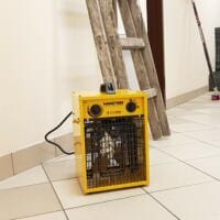 Renovierung: Gelber Master B 3.3 EPB Heizlüfter an Wand mit Leiter. Baustelle mit Fliesenboden. Heizgerät für Renovierungsarbeiten.