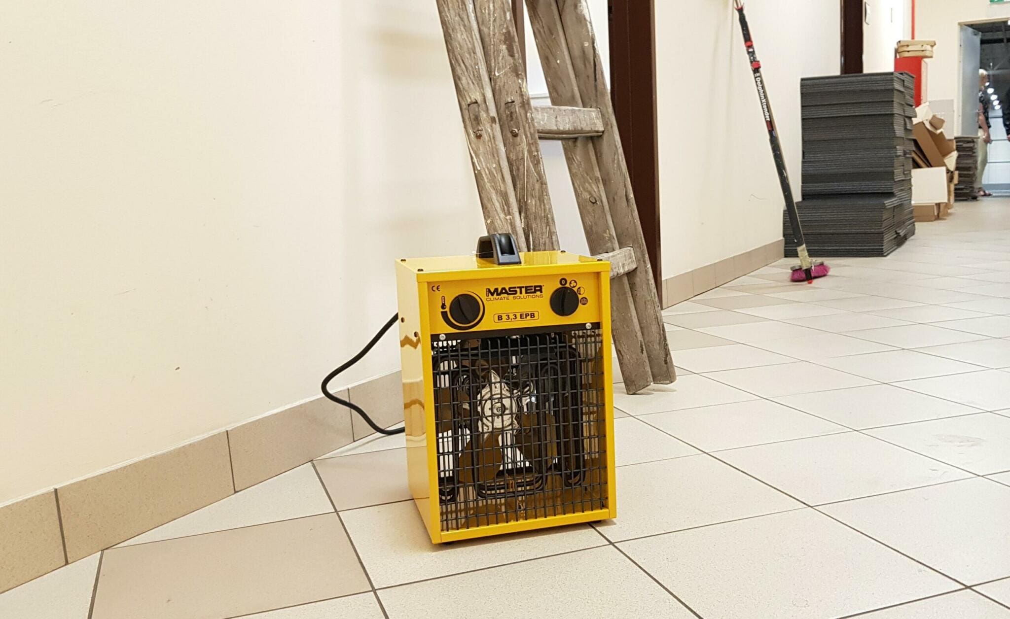 Renovierung: Gelber Master B 3.3 EPB Heizlüfter an Wand mit Leiter. Baustelle mit Fliesenboden. Heizgerät für Renovierungsarbeiten.