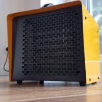 Gelber Master B 3PTC Heizlüfter auf Holzboden. Kompakter, tragbarer Heizlüfter mit schwarzem Gitter und Griff. Heizgerät für Werkstatt/Garage.