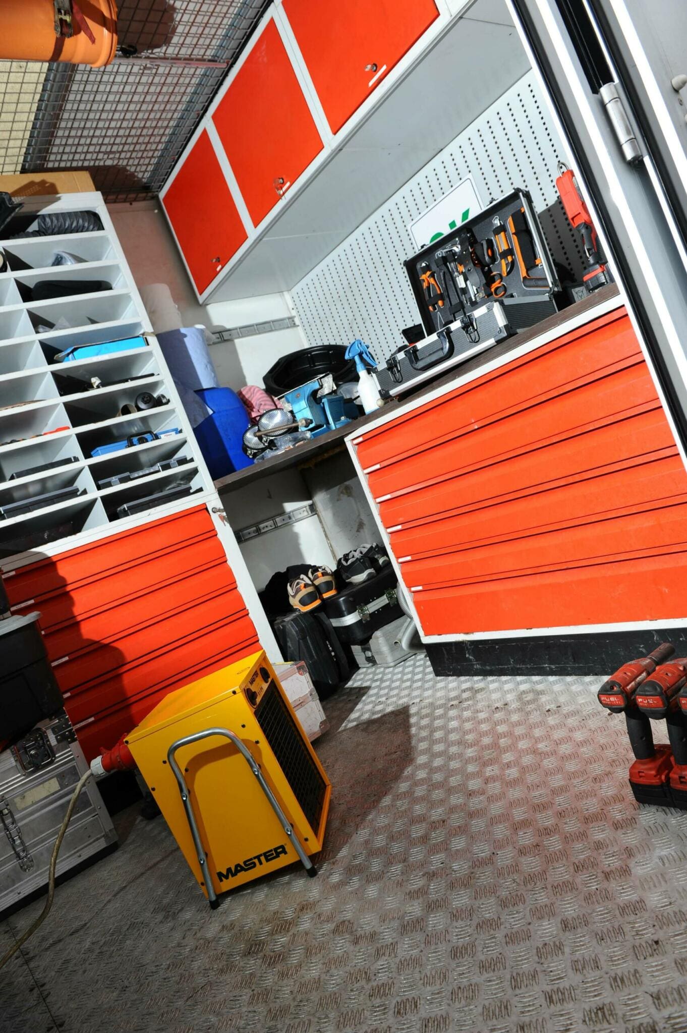 Innenansicht eines Master Containers: Werkzeug, Regale und Schränke in Orange. Werkstatt-Equipment auf geriffelter Metalloberfläche.