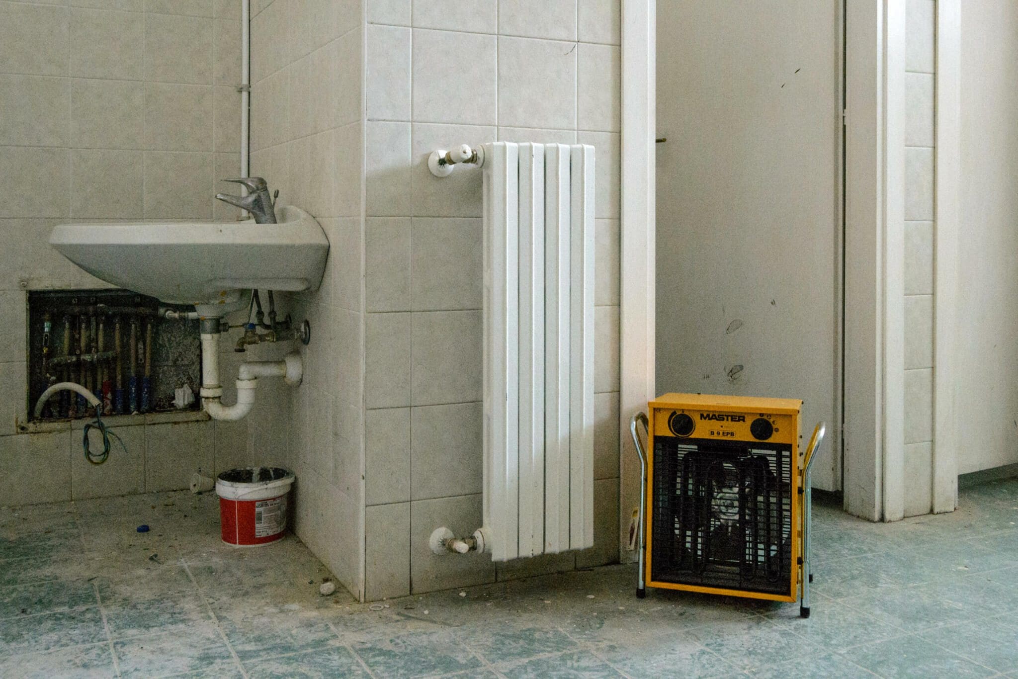 Renovierung eines Badezimmers mit Waschbecken, Heizkörper und gelbem Master-Heizlüfter. Fliesen an Wand und Boden.