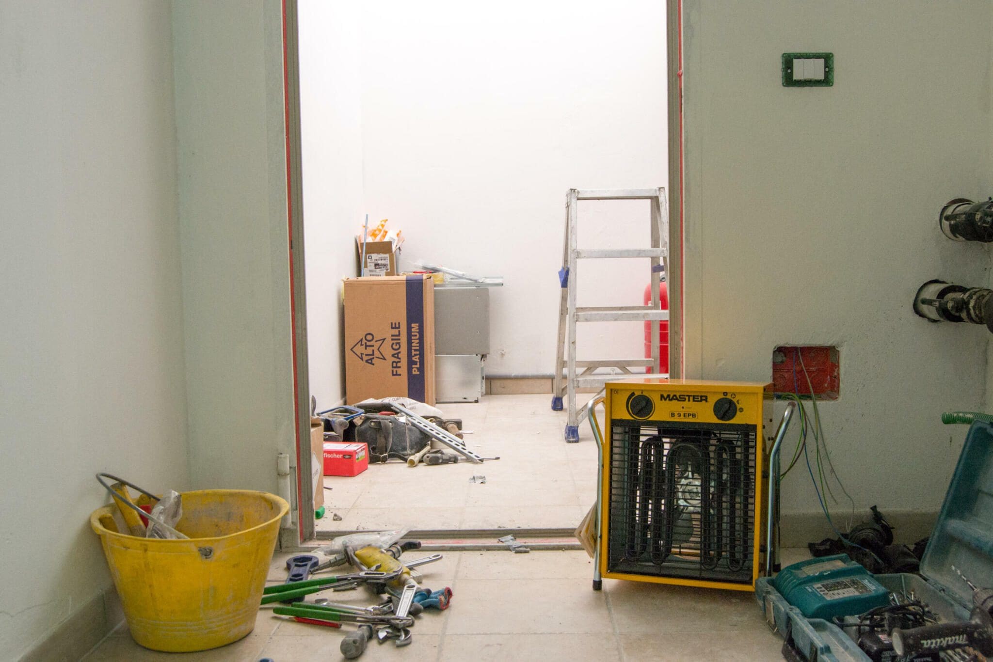 Renovierung: Baustelle mit Werkzeug, Leiter und Master B-9 Heizlüfter. Raum im Umbau mit Karton und Eimer.