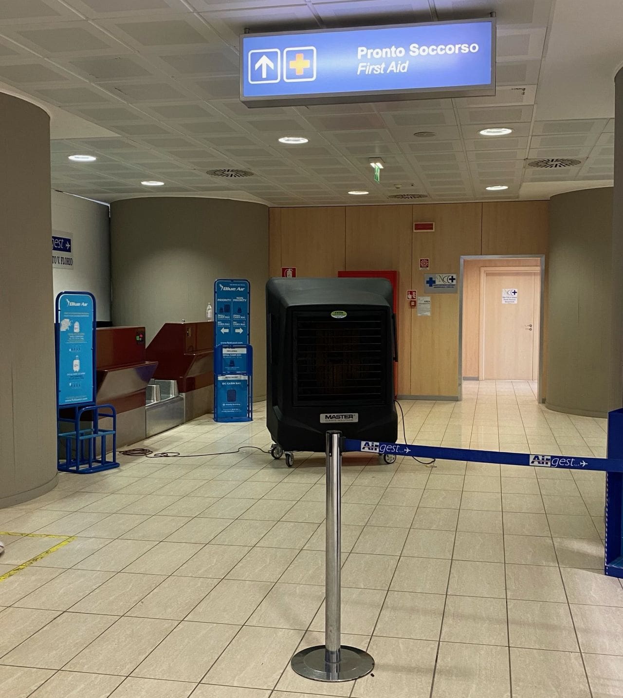 Flughafen: Master-BC-221 vor Erste-Hilfe-Station. Schild Pronto Soccorso/First Aid. Kühler und Absperrband. Wartebereich im Terminal.