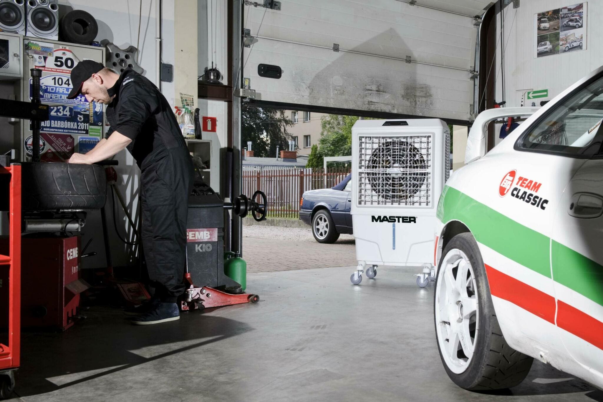 Werkstatt-Szene: Mechaniker bei der Reifenmontage, MASTER BC 80 Luftkühler im Hintergrund. Auto-Service mit Kühlung.