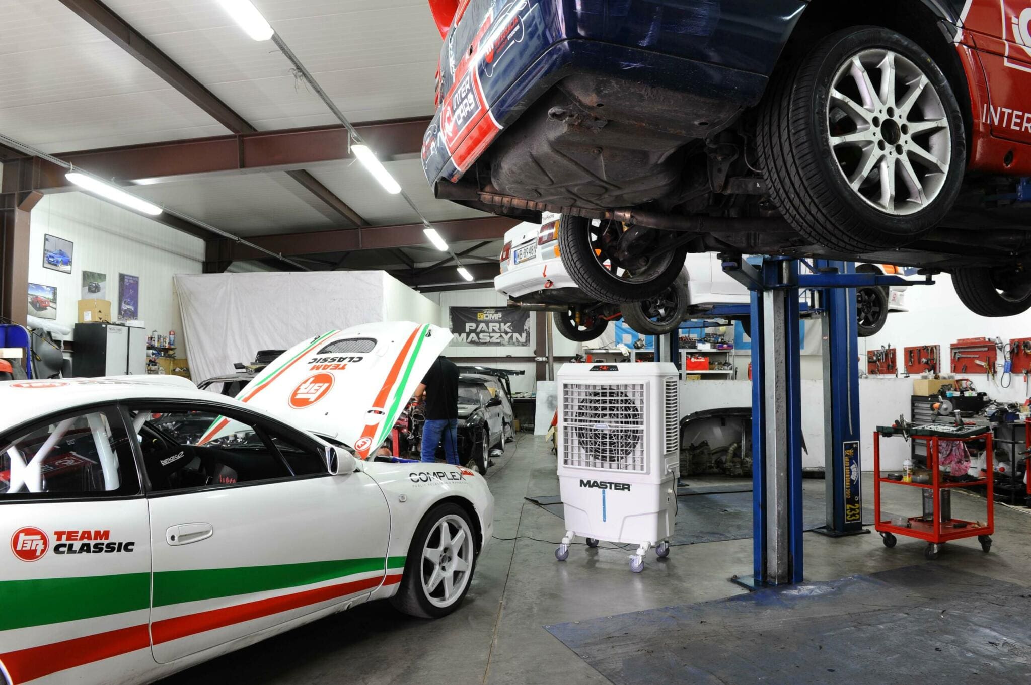 Innenaufnahme einer Werkstatt mit Autos auf Hebebühnen und einem Master BC-80 Klimagerät. Autoservice im Fokus.