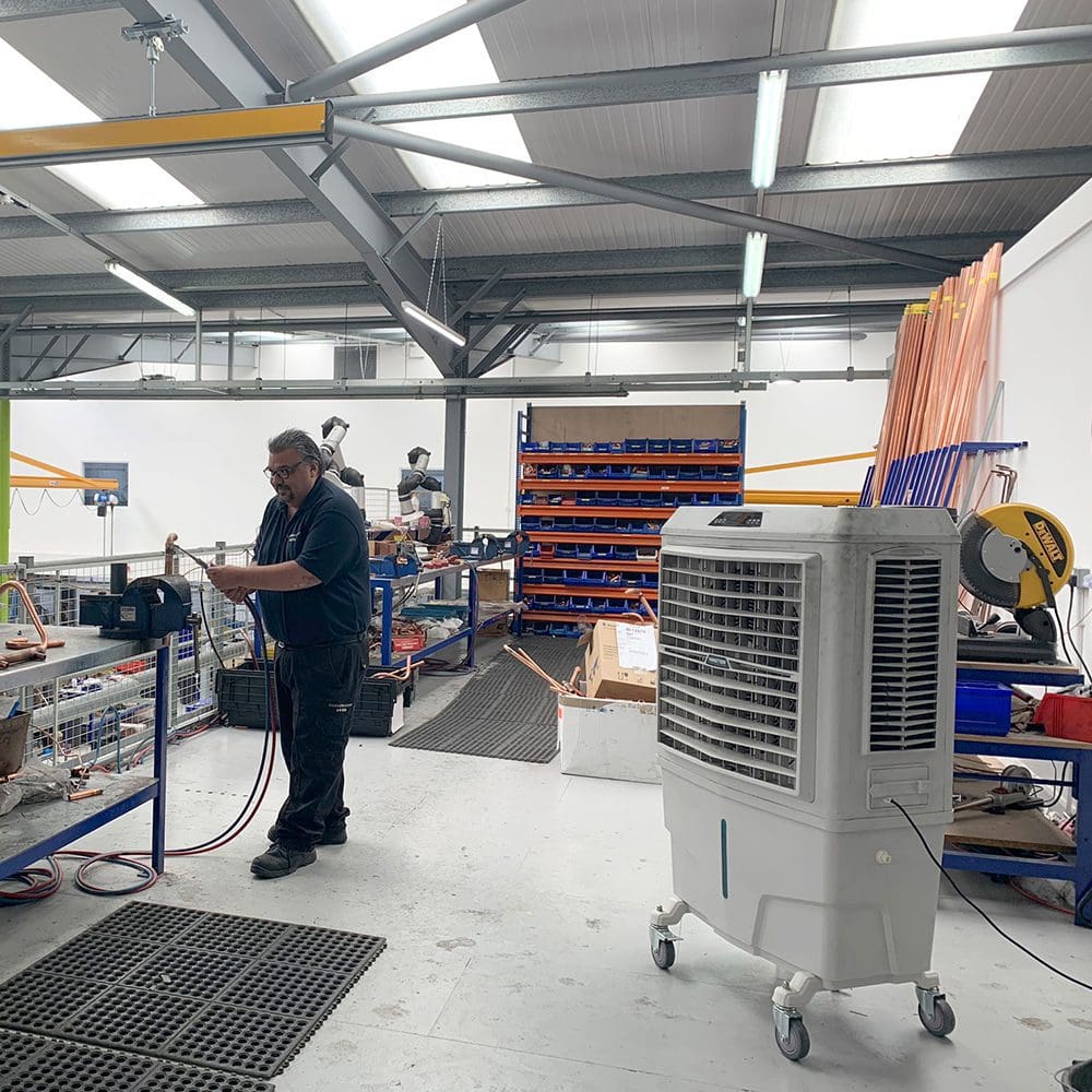 Master BC-80 Fabrik: Arbeiter in Werkstatt mit Klimaanlage, Werkzeugen und Rohren. Metallregale im Hintergrund. Industrielle Fertigung.
