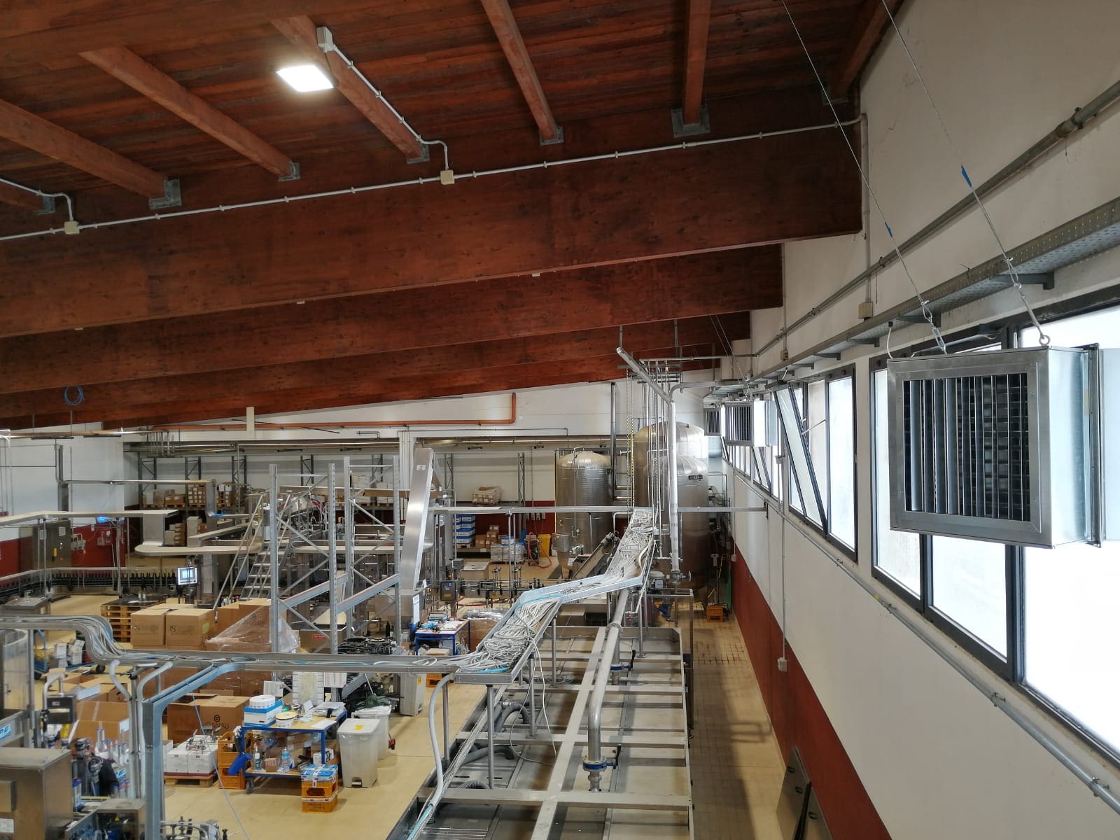 Innenansicht: Master-BCM-Lüftungskanäle in einer Produktionshalle. Holzdecke, Fensterreihe und Förderbandanlage. Industrielle Lüftungstechnik.