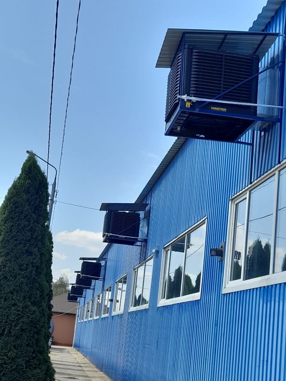 Master BCM Wandmontage: Vertikale Ansicht von Kühlgeräten an einer blauen Gebäudewand mit Fenstern. Kühlsystem Installation.