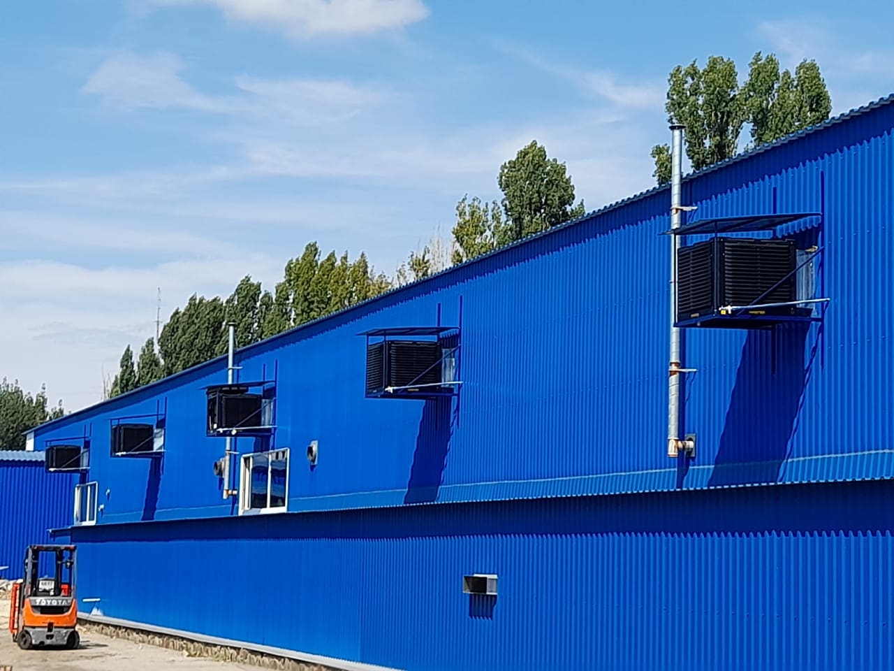 Blaue Lagerhalle mit Kühlwand-Installation. BCM Master Kühlsysteme an der Wand montiert. Stapler im Vordergrund.