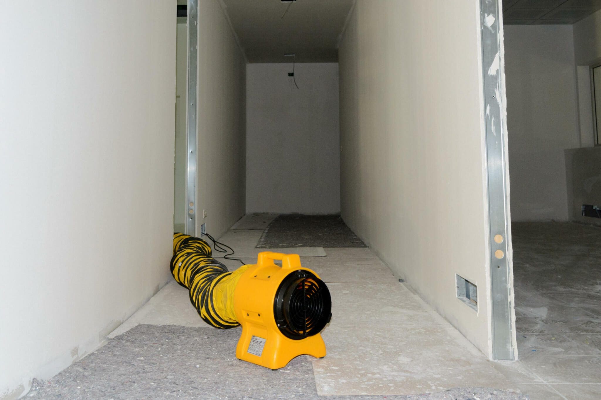 Baustelle: Gelber Ventilator mit Schlauch in einem Raum im Rohbau. Master BL 4800 Bautrockner zur Trocknung.