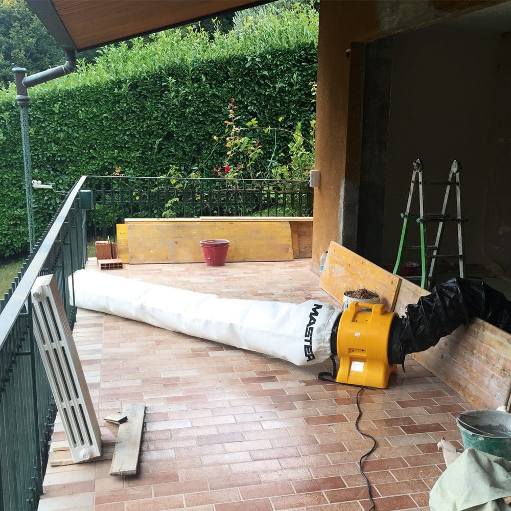 Master BL-4800 Bautrockner mit Staubbeutel auf einer Terrasse. Gelber Bautrockner mit weißem Sack. Bauarbeiten im Hintergrund.