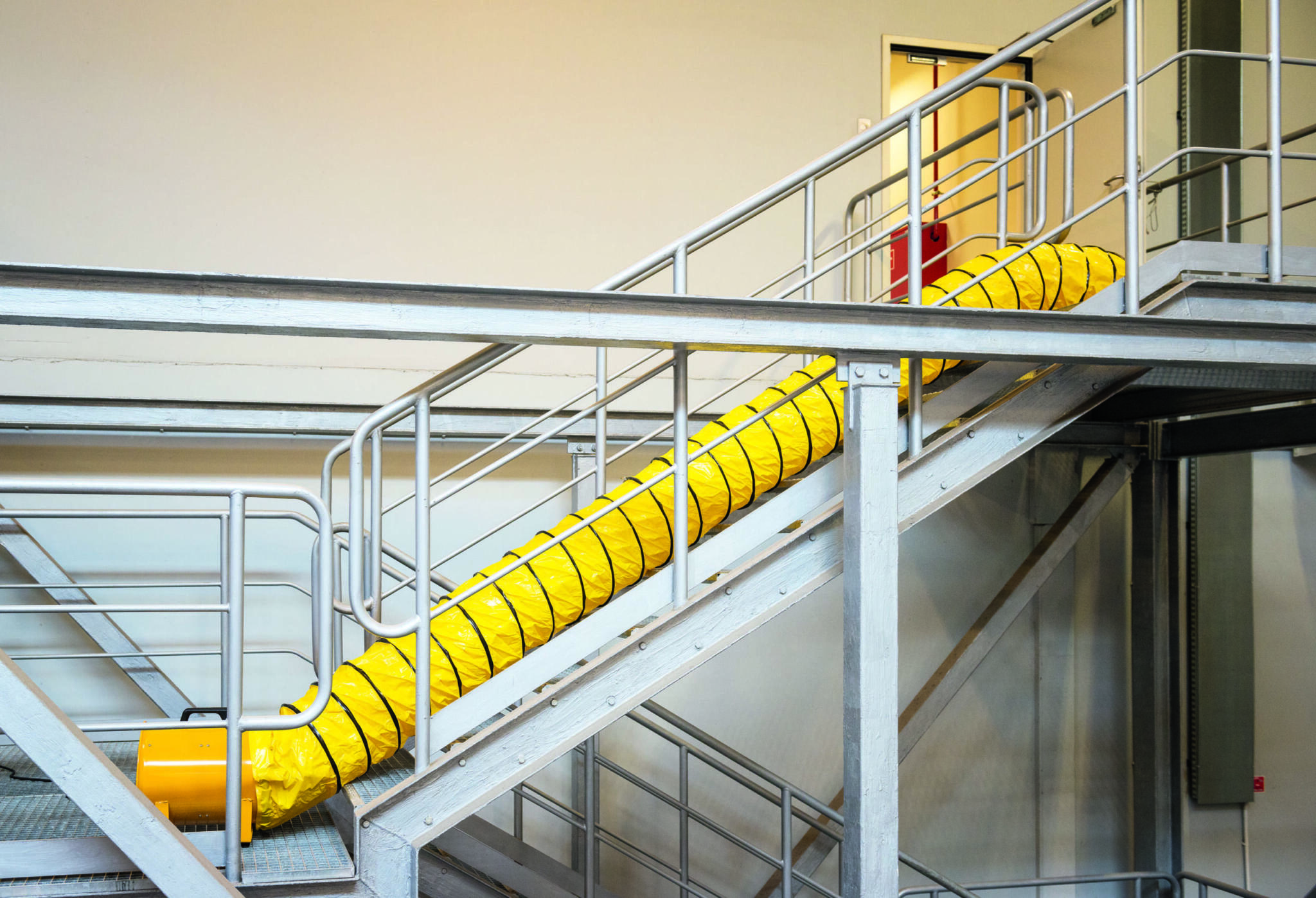Gelber Lüftungsschlauch auf Treppe im Lager. Master-BLM-4800 Gebläse für Belüftung. Arbeitsplatzsicherheit im Warenhaus.