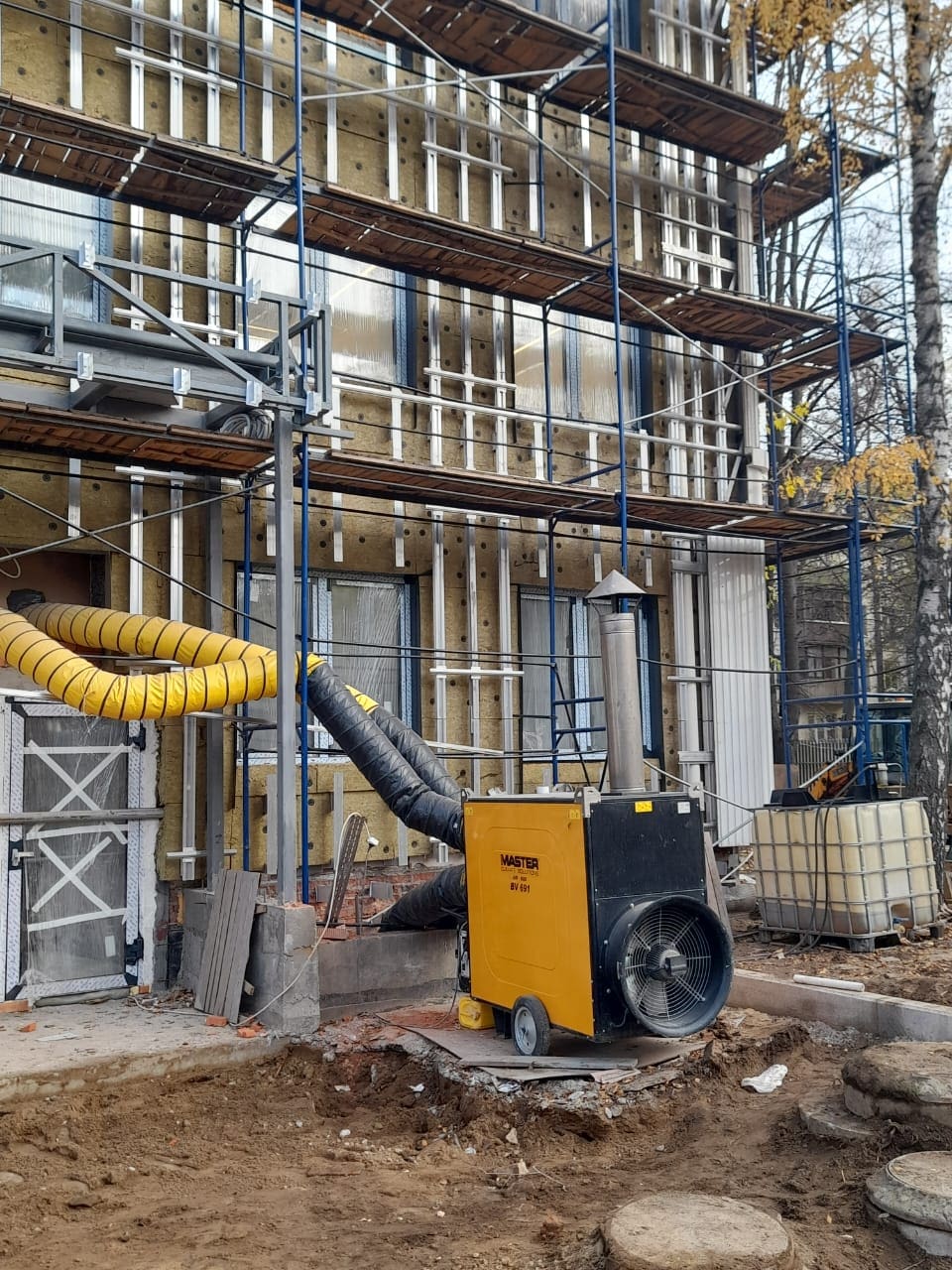 Baustelle: Gebäudeisolierung mit Gerüst. Master BV 691 Heizgerät liefert Wärme von außen. Baukonstruktion im Detail.