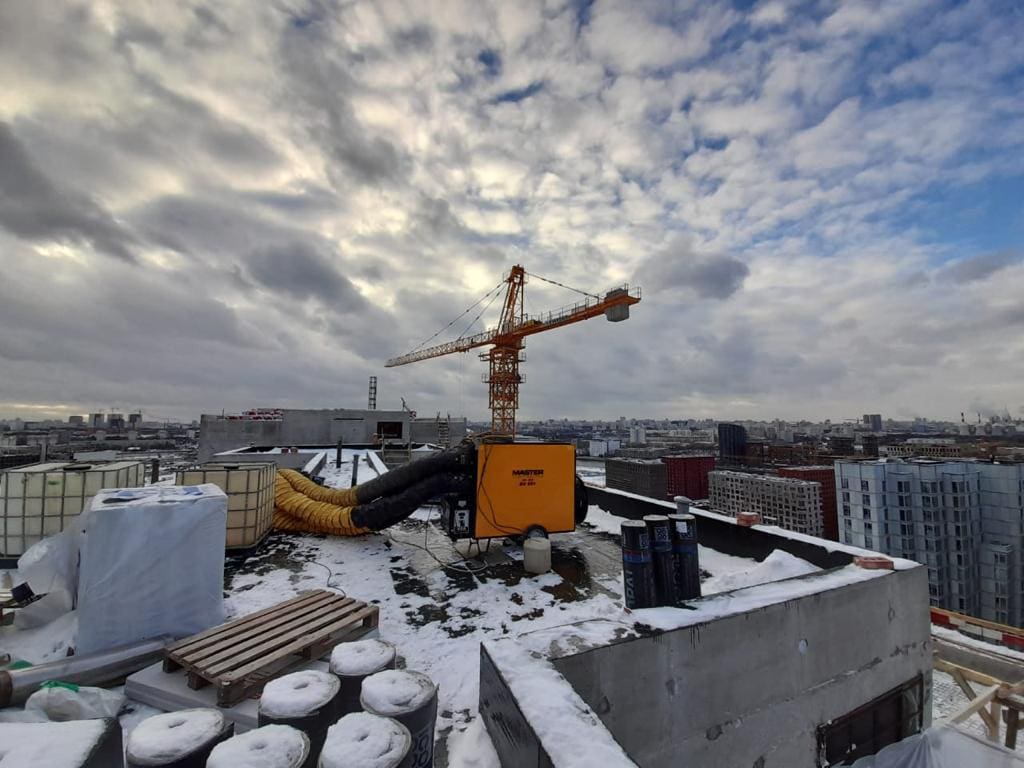 Baustelle auf dem Dach mit Kran und Bauausrüstung. Master-BV-691 im Einsatz, Bauarbeiten im Winter. Schnee bedeckt die Baustelle.