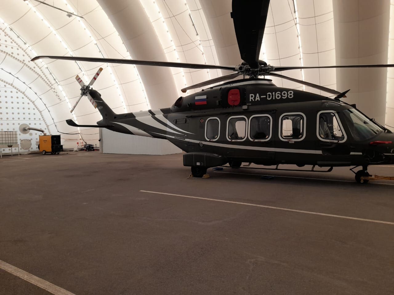 Schwarzer Hubschrauber im Flugzeughangar mit pneumatischer Heizung. Flugzeugwartung im Hangar. Flugzeugbau und -technik.