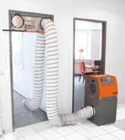 Heylo DCS PF3500 Bautrockner: Luftentfeuchter mit Schlauch in Türrahmen, orange-graues Gehäuse im Raum.