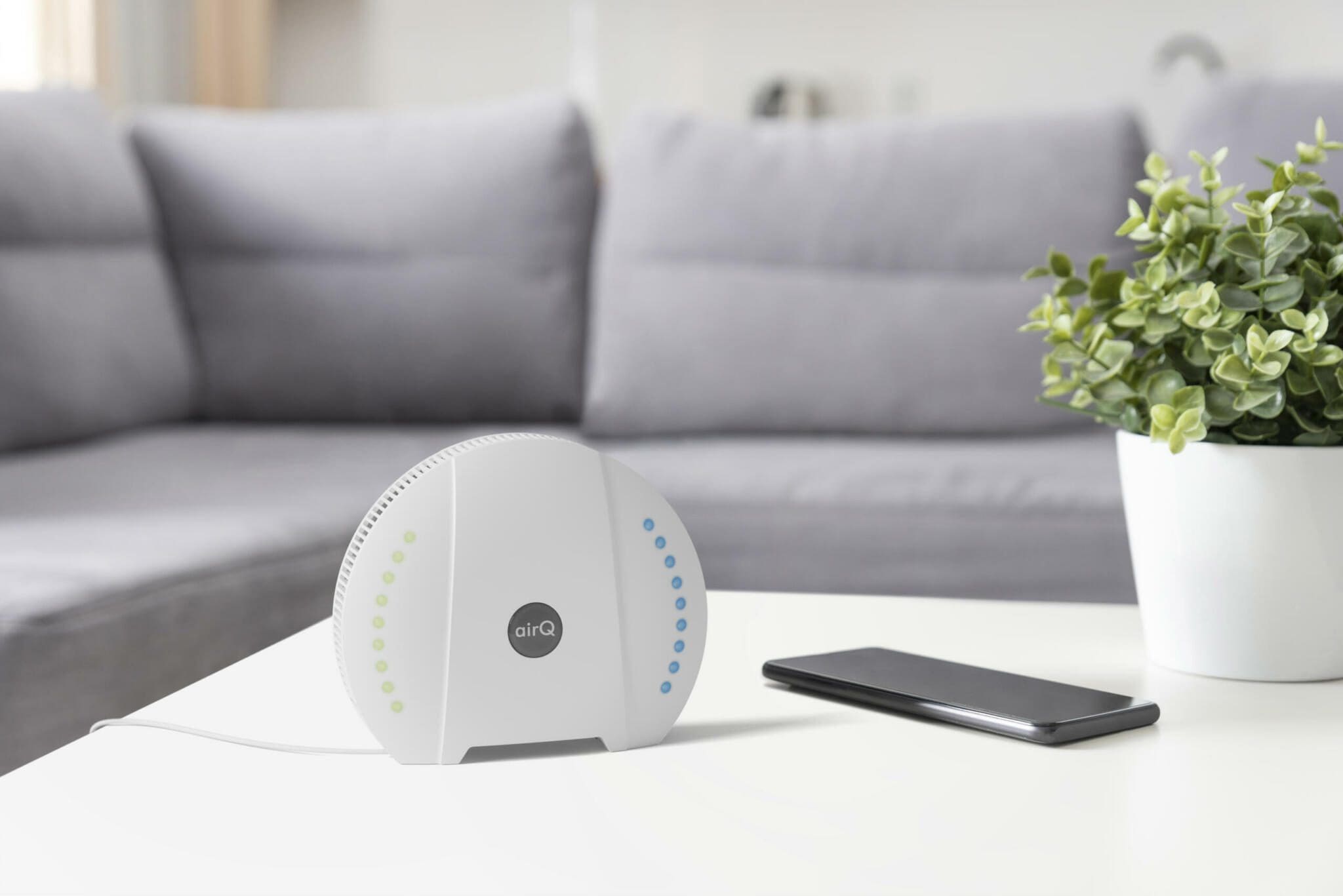 air-Q Raumluftmessgerät im Wohnzimmer. G.A.Luft Luftreiniger für gesunde Raumluft. Handy neben Gerät.