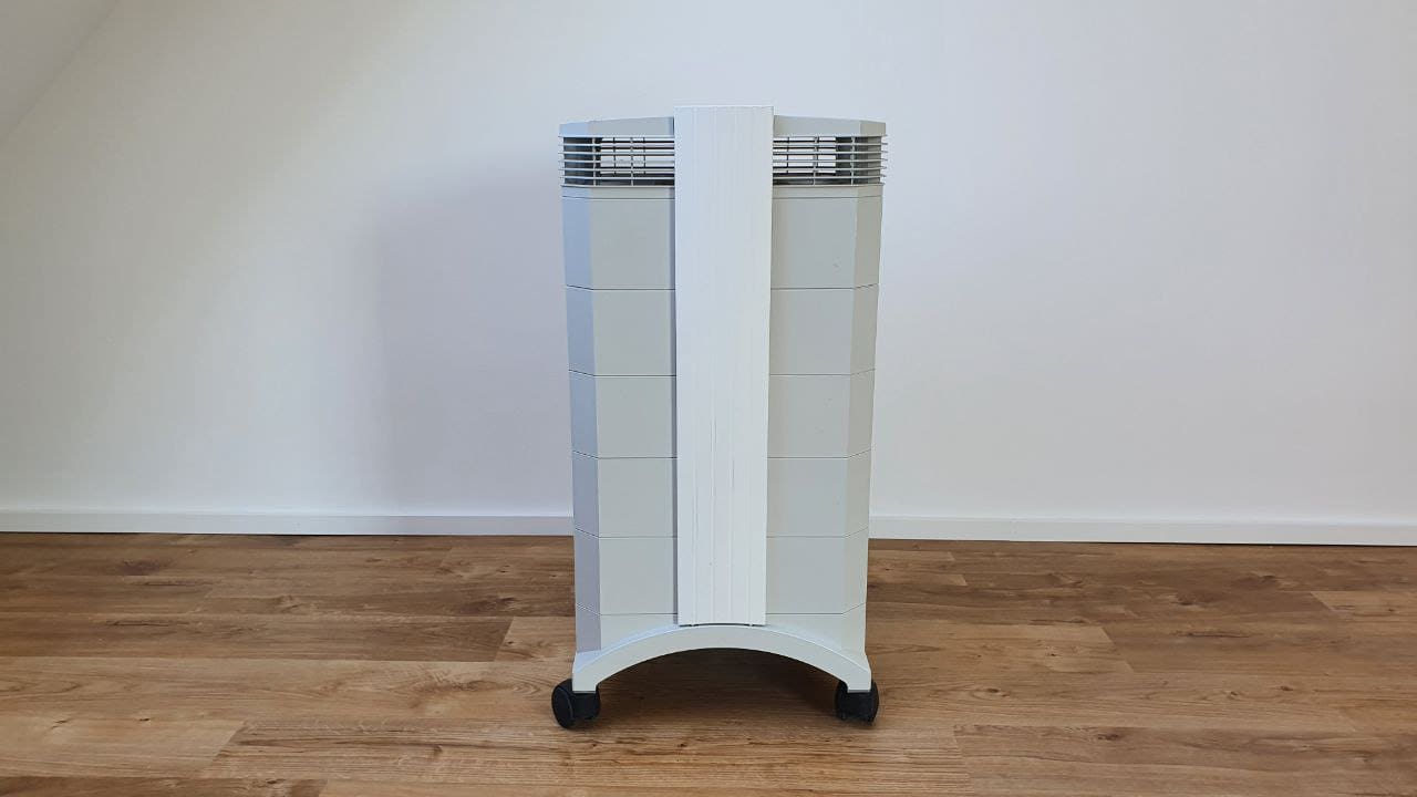 Der IQAir HealthPro 250 Luftreiniger, stehend auf einem Holzboden vor einer weißen Wand, bietet fortschrittliche Luftreinigungstechnologie.