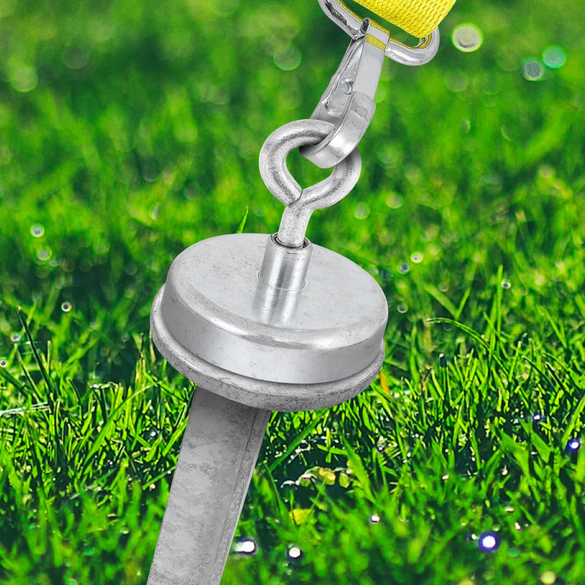 Teller Hering 400mm im Gras: Detailaufnahme eines robusten Erdankers mit gelbem Gurt. Ideal für sicheren Halt im Outdoor-Bereich.