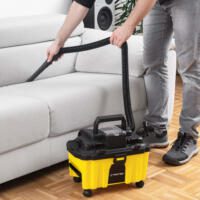 Akku-Staubsauger VC-15-20V im Einsatz: Eine Person saugt mit dem gelb-schwarzen Fugendüse-Aufsatz ein weißes Sofa ab. Ideal für die Reinigung!